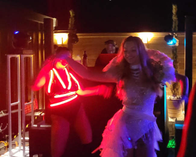 Two performers are dancing on a stage illuminated by colorful lights at a nighttime event.
