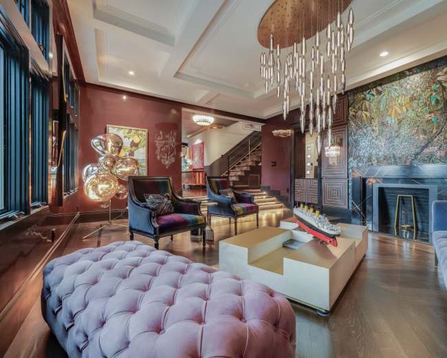 The image showcases a luxurious living room featuring velvet sofas, a large chandelier, and a decorative wall with a nature mural.