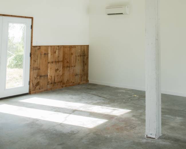 The image features an empty room with white walls, a wooden accent wall, a ceiling light fixture, and an air conditioning unit.