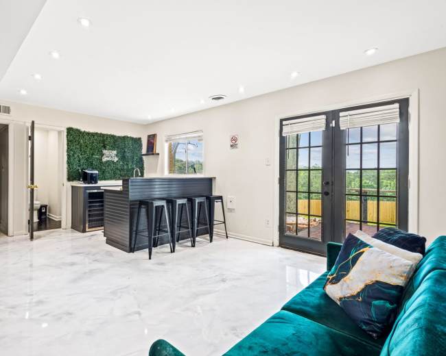 The image shows a modern living space featuring a marble floor, a green accent wall, a black kitchen island with stools, and large glass doors leading to an outdoor view.