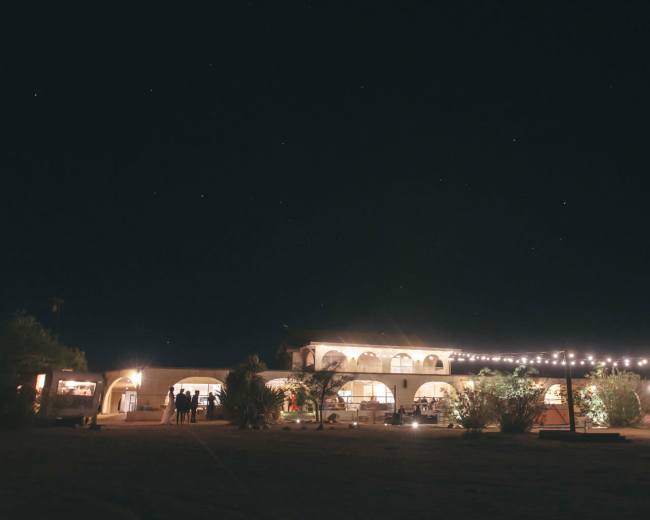 A well-lit building with multiple arches stands under a starry night sky, surrounded by trees and string lights.