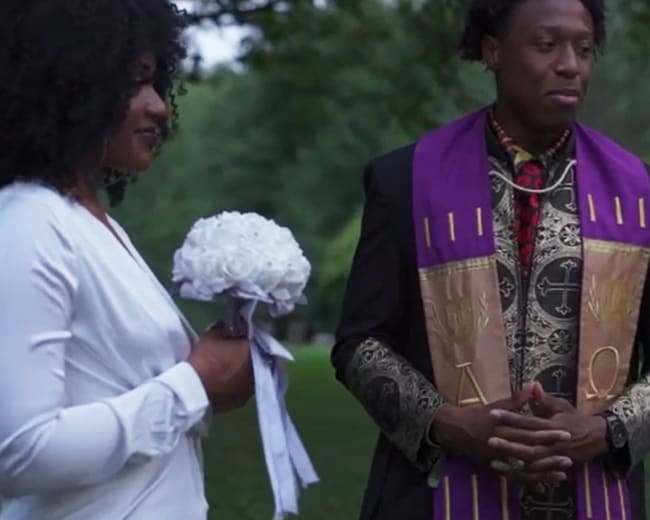 A woman in a white dress holds a bouquet while standing next to a man in traditional ceremonial attire.