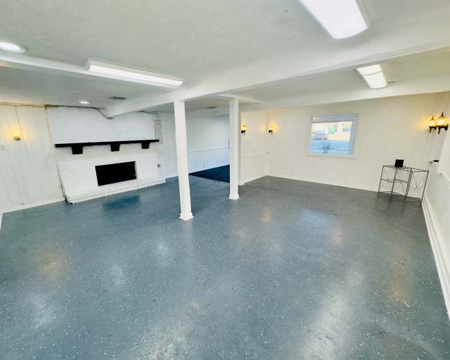 A spacious room with a white brick fireplace, light-colored walls, and a gray speckled floor.