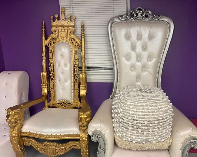 The image shows two ornate chairs side by side: a gold throne with a crown design on the back and a plush silver chair with tufted upholstery.