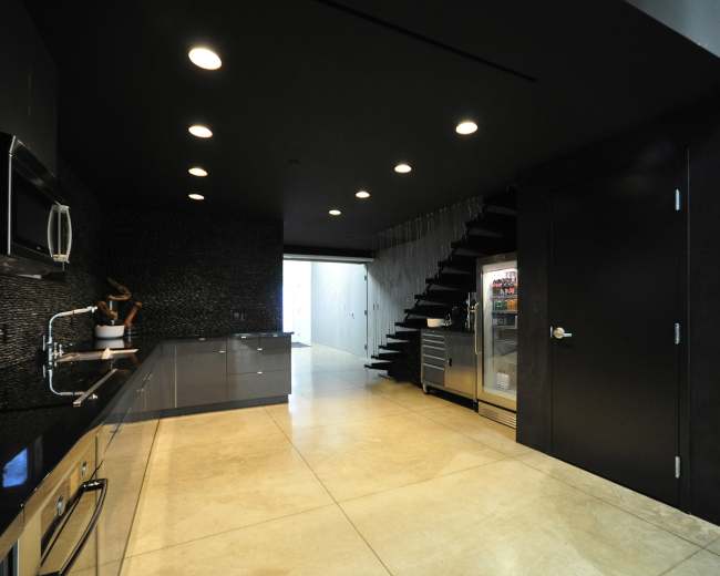 A modern kitchen with dark cabinetry, stainless steel appliances, and a staircase leading to an upper level.