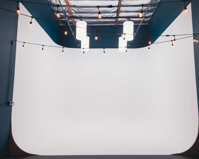 The image shows a spacious photo studio with a curved white backdrop and pendant lights hanging from the ceiling.