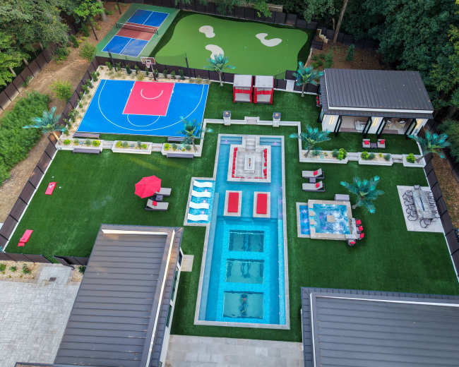 The image shows a spacious outdoor area featuring a swimming pool, a basketball court, a putting green, and various seating arrangements surrounded by landscaping.