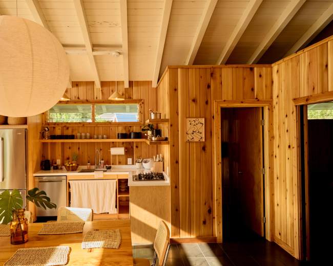 The image shows a wooden kitchen and dining area featuring a round paper lantern, a stainless steel refrigerator, and a dining table with woven placemats.