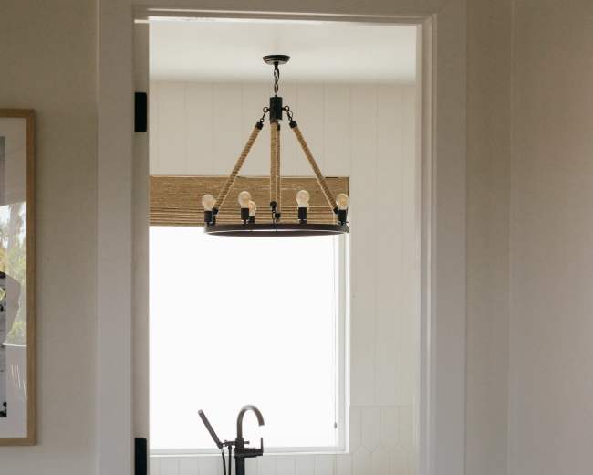 A modern bathroom features a freestanding tub, a window with natural light, and a stylish chandelier above.