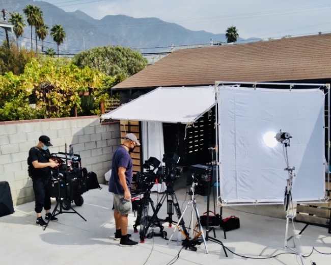 A film crew sets up equipment in an outdoor location with mountains in the background.