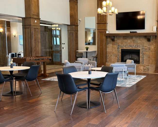 The image shows a spacious indoor lounge area with tables and chairs, a fireplace, large mirrors, and a television mounted on the wall.