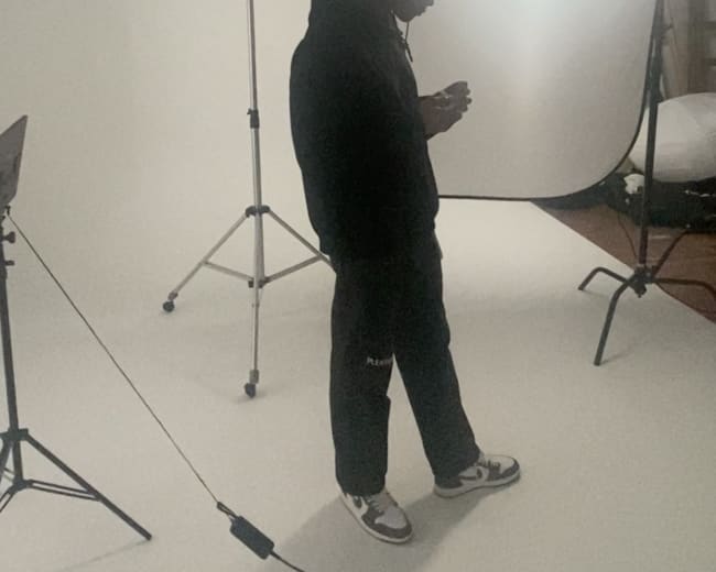 A person stands in a photography studio, framed by a white backdrop and lighting equipment.