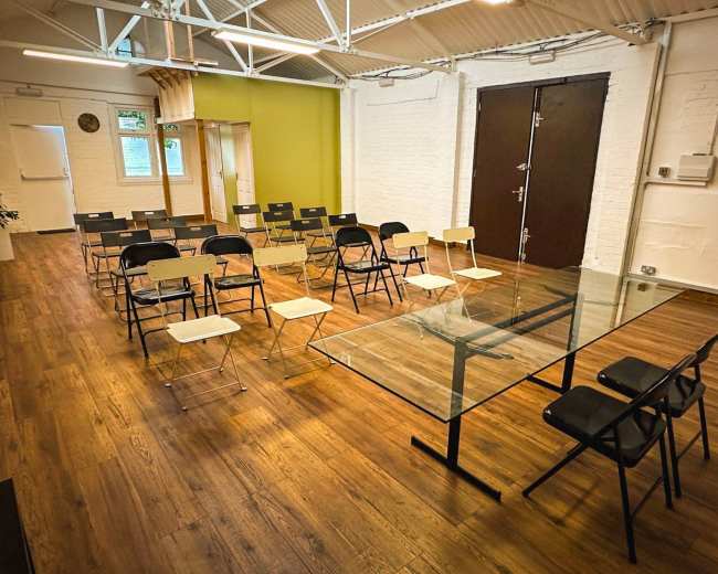 A modern meeting room features a glass table surrounded by black and white chairs, with additional seating arranged in rows.