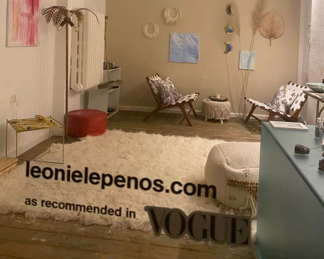 The image shows a modern, minimalist interior featuring a large white rug, a light-colored wall with decorative wall hangings, and contemporary furniture arranged in a cozy setting.