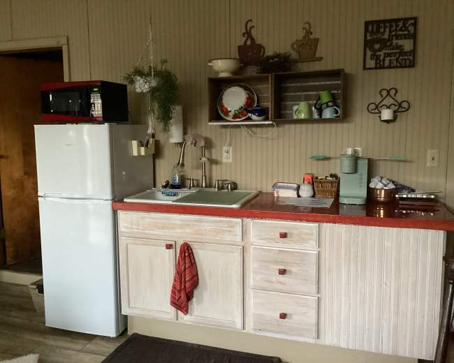 The image shows a kitchen area with a white refrigerator, a red countertop, and various utensils and dishes displayed on shelves.