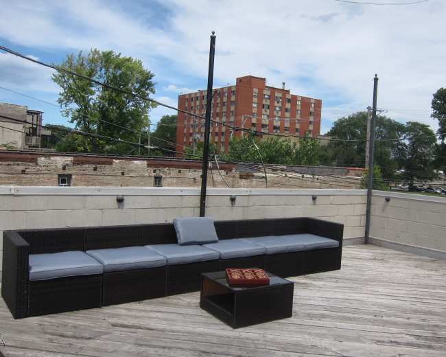 The image shows a rooftop area with a sectional couch and a small table made of wicker, surrounded by a concrete wall and power lines above.