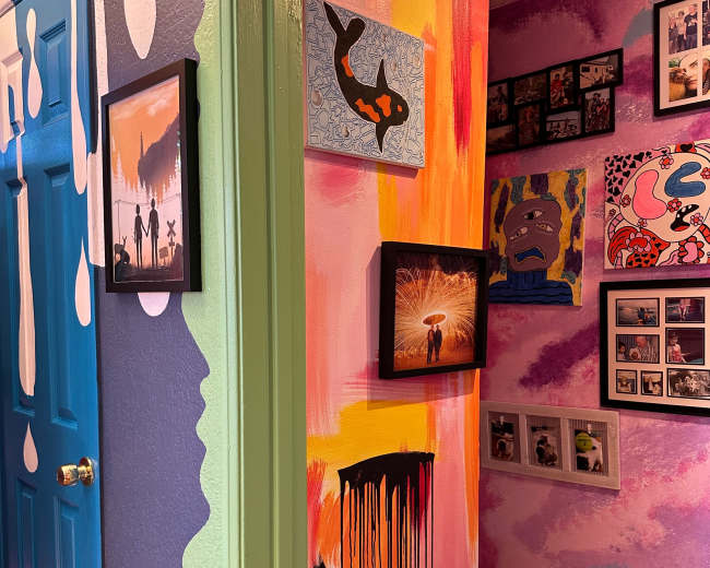 The image shows a brightly painted hallway with artwork framed on the walls, including photos and colorful paintings.