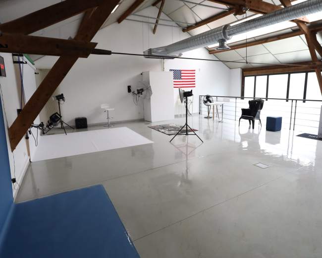 A spacious photography studio with wooden beams, a white backdrop, lighting equipment, and an American flag displayed on the wall.