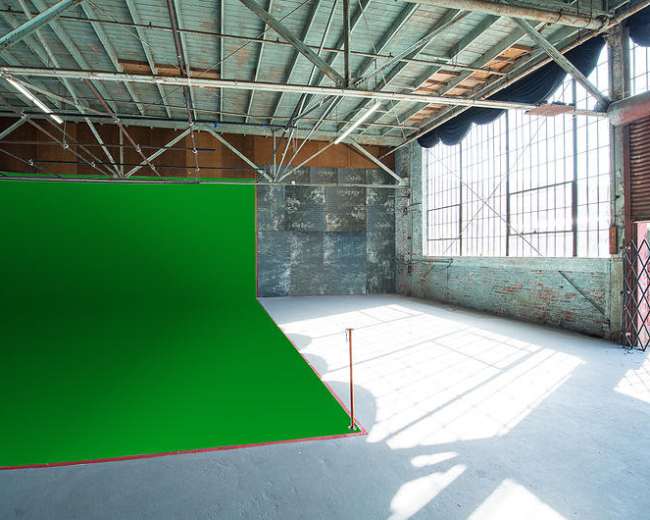 The image shows a spacious studio with a green backdrop, large windows, and exposed beams.