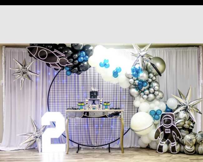 A festive decoration setup featuring a large number "2," a dessert table adorned with themed treats, and a backdrop of balloons and star decorations.