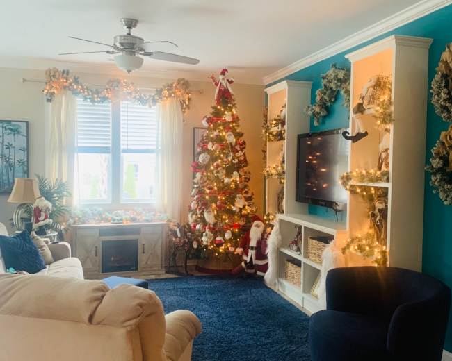 The living room features a decorated Christmas tree, a cozy armchair, and a wall-mounted television with festive decorations.