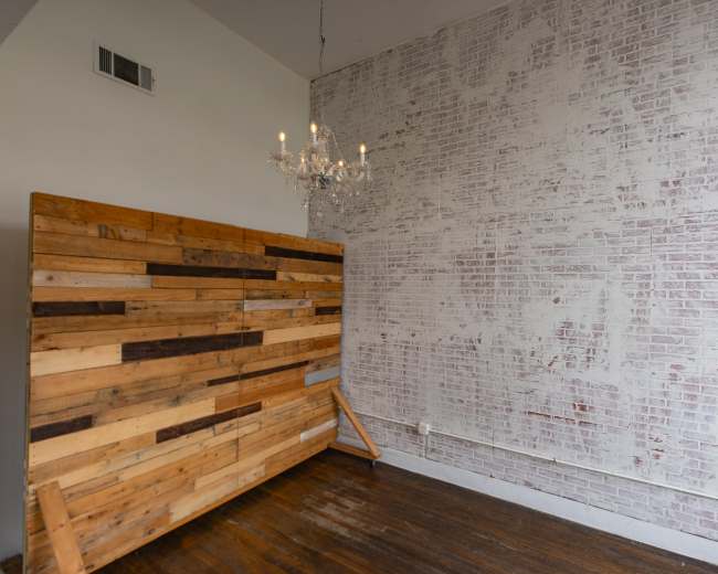 The image shows a room with a wooden accent wall on the left, a white brick wall on the right, and a chandelier hanging from the ceiling.