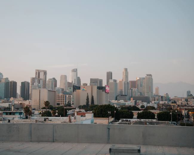 The image shows a panoramic view of the Los Angeles skyline with modern skyscrapers and commercial buildings under a clear sky.