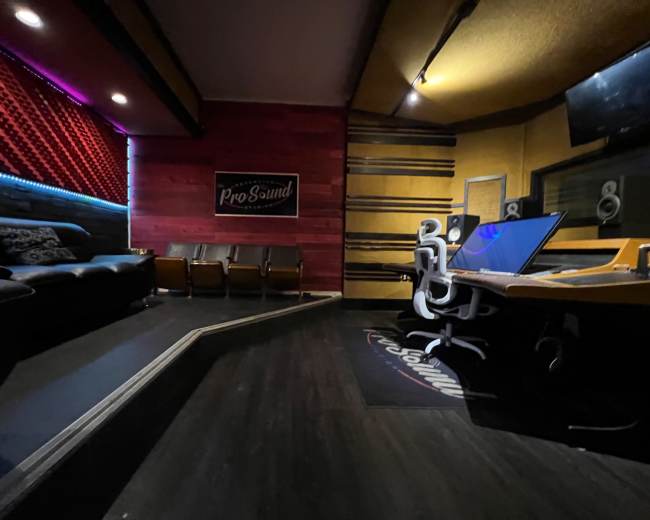 The image shows an interior of a recording studio with a seating area, a mixing desk, and colorful accent lighting on the walls.
