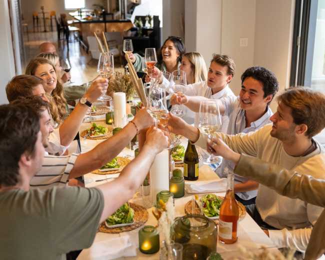 A group of people is gathered around a dining table, raising their glasses in a toast while enjoying a meal.