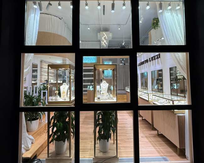 The image shows a jewelry store with display cases filled with various pieces, viewed through large windows framed by a black exterior.