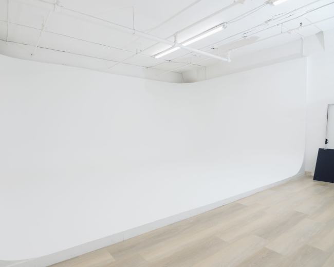 The image shows a spacious studio with a smooth, white curved wall and wooden flooring.