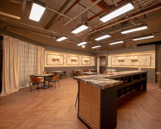 The image shows a spacious dining area with a large island countertop, several tables, and wall-mounted light fixtures illuminating the space.