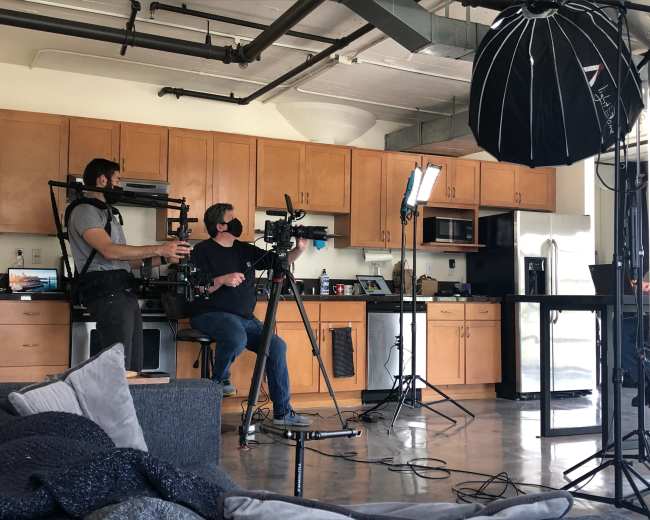 A film crew sets up equipment in a modern kitchen for a video shoot.