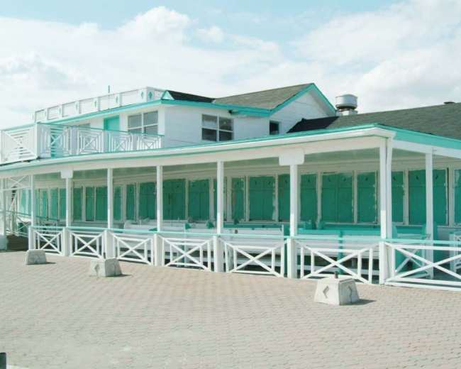 A coastal building with turquoise trim and white wooden structures on a paved surface.