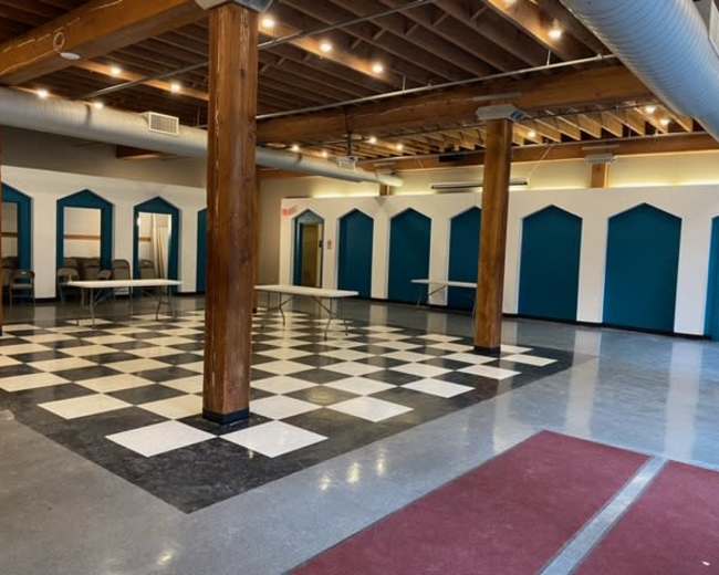 An empty indoor space with a checkered floor, wooden columns, and blue-tinted archways along the walls.