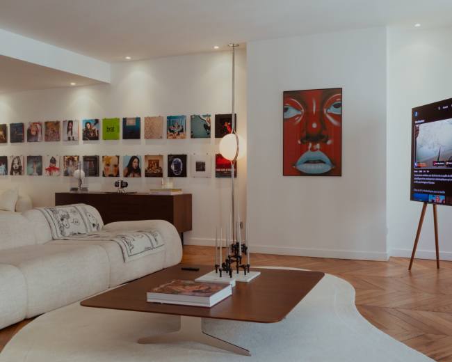 The living room features a modern sofa, a coffee table with a magazine, wall art, and a TV displaying streaming content.