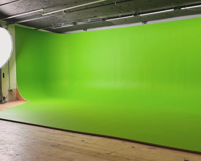 The image shows a bright green studio backdrop in an empty room with wooden flooring.