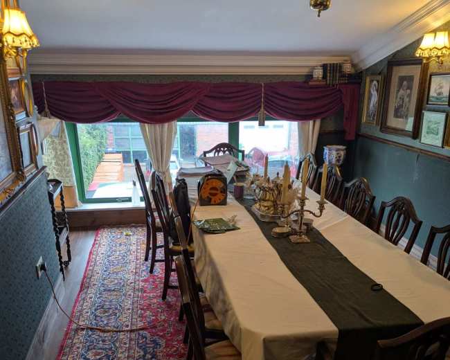 A long dining table is set with a green runner in a room decorated with framed pictures and a large window displaying greenery outside.