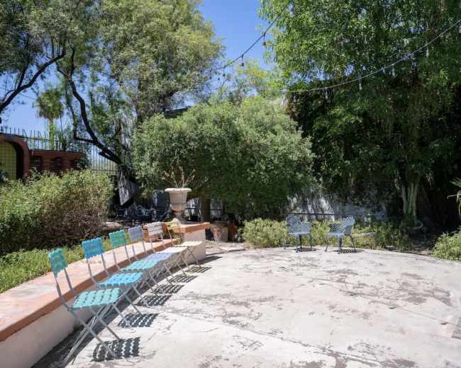 The image shows a patio area with several turquoise folding chairs arranged in a row, surrounded by greenery and a concrete surface.