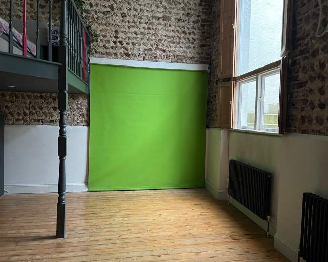 The image shows a room with exposed brick walls, a green backdrop, a wooden floor, and a lofted bed.