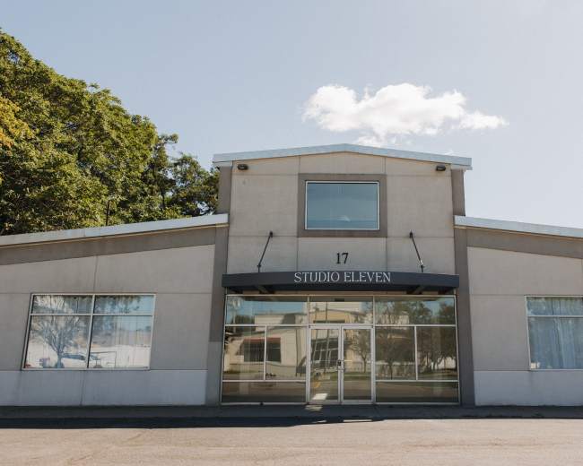 The image shows a modern, rectangular building with large glass windows and a sign that reads "STUDIO ELEVEN" above the entrance.