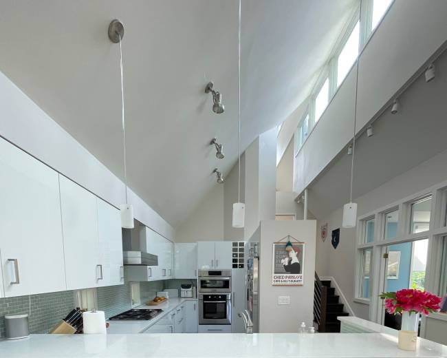 The image shows a modern kitchen with white cabinetry, stainless steel appliances, and three wooden bar stools arranged at a counter.