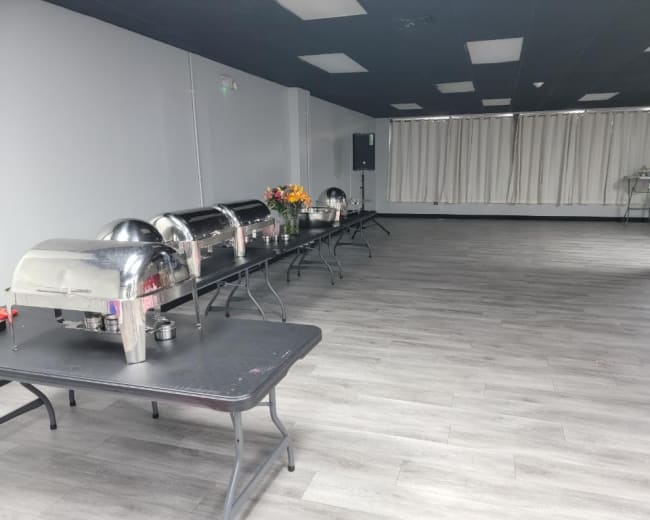 A spacious room with several chafing dishes set on long tables, arranged neatly and surrounded by a lightly decorated space.