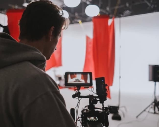 A person operates a camera in a studio with red backdrops and bright lighting.