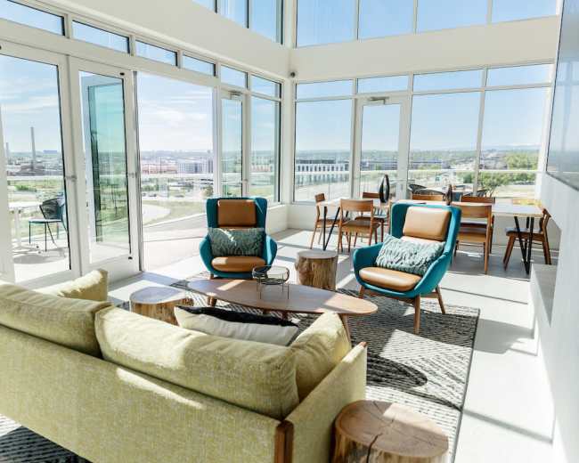 The image shows a modern lounge area with large windows, featuring two chairs and a sofa arranged around a coffee table with a view of the city.