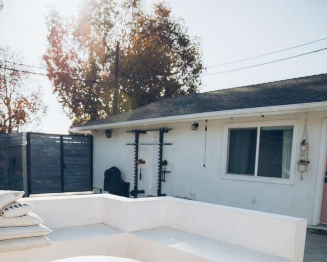 The image shows a backyard area with a circular fire pit surrounded by a white, built-in seating arrangement and a house in the background.