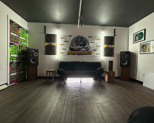 The image shows a music studio with a black couch, large speakers, and various decorations on the walls.