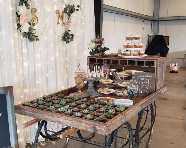 A dessert table adorned with various treats and a welcome sign for a bridal shower is set against a backdrop of fairy lights and floral decorations.