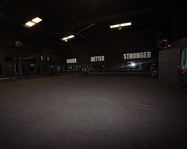 The image shows an empty gym with a black rubber floor and motivational phrases on the wall.