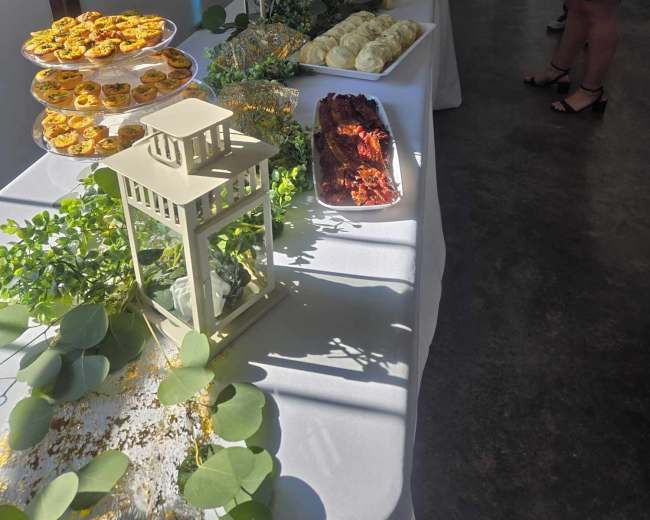 A long table is set up with a variety of food items and decorative lanterns, with a person standing nearby.